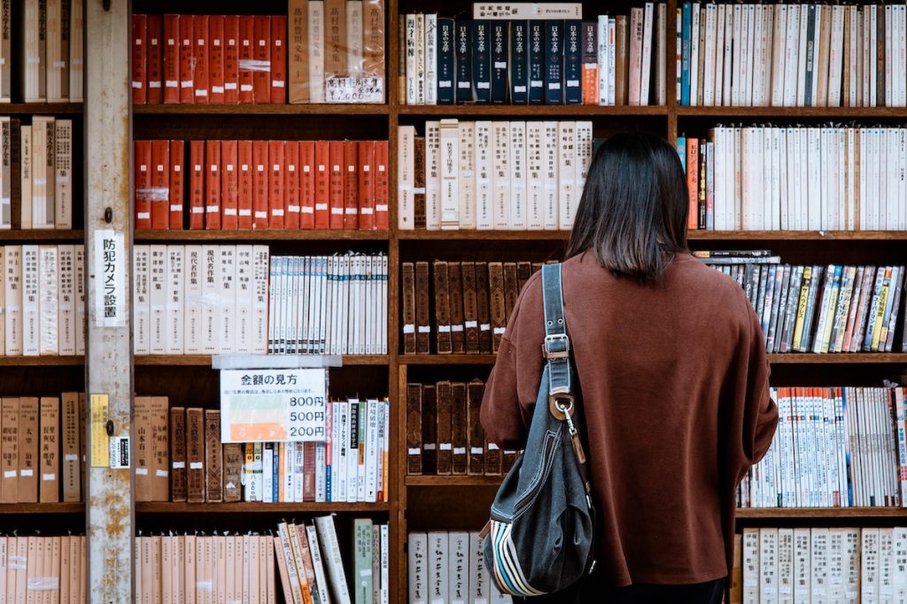 oman Wearing Brown Shirt Carrying Black Leather Bag on Front of Library Books